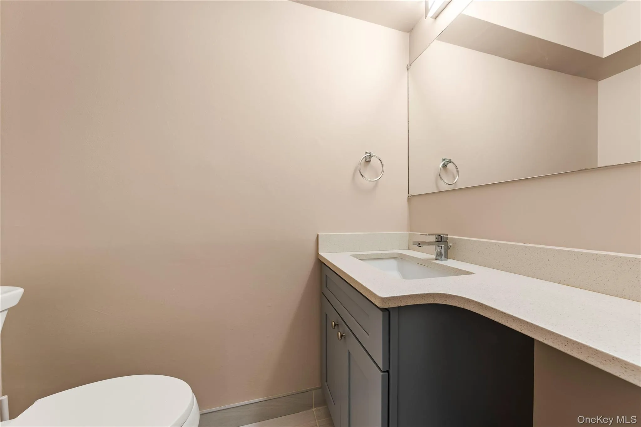 Vanity with integrated sink, light-toned countertop, dark-toned cabinetry, and wall-mounted mirror Vanity with integrated sink, light-toned countertop, dark-toned cabinetry, and wall-mounted mirror