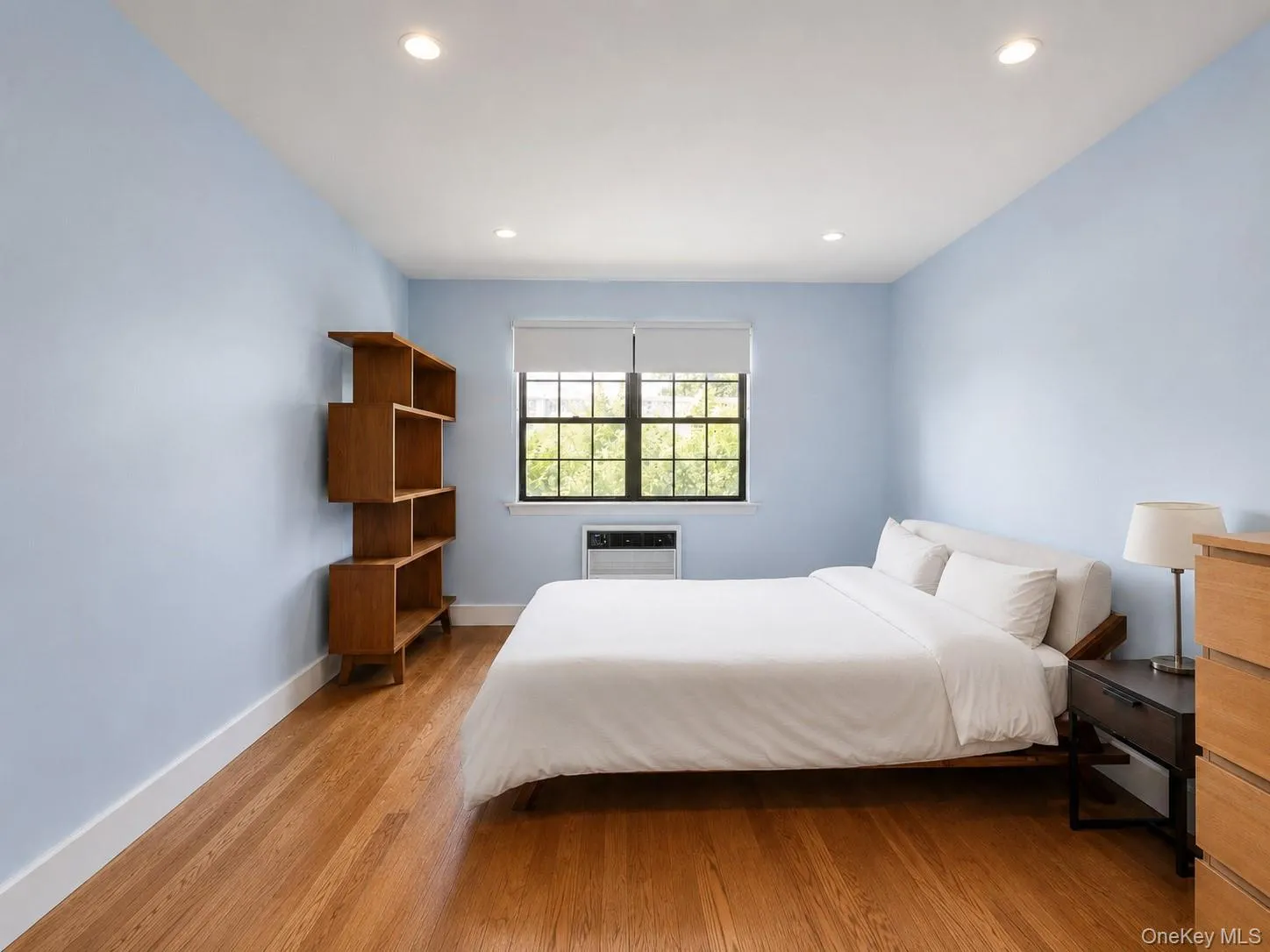 Hardwood flooring with recessed lighting, light blue walls, and a window with a built-in air conditioning unit Hardwood flooring with recessed lighting, light blue walls, and a window with a built-in air conditioning unit