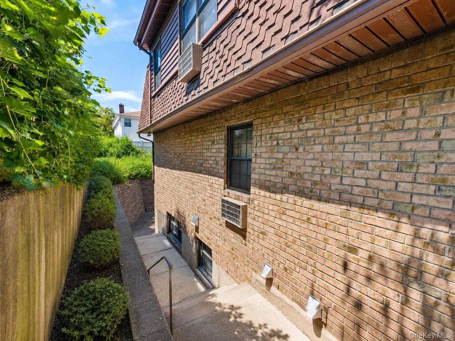 Brick exterior with a window unit, a lower-level window, and a concrete staircase featuring a metal handrail Brick exterior with a window unit, a lower-level window, and a concrete staircase featuring a metal handrail