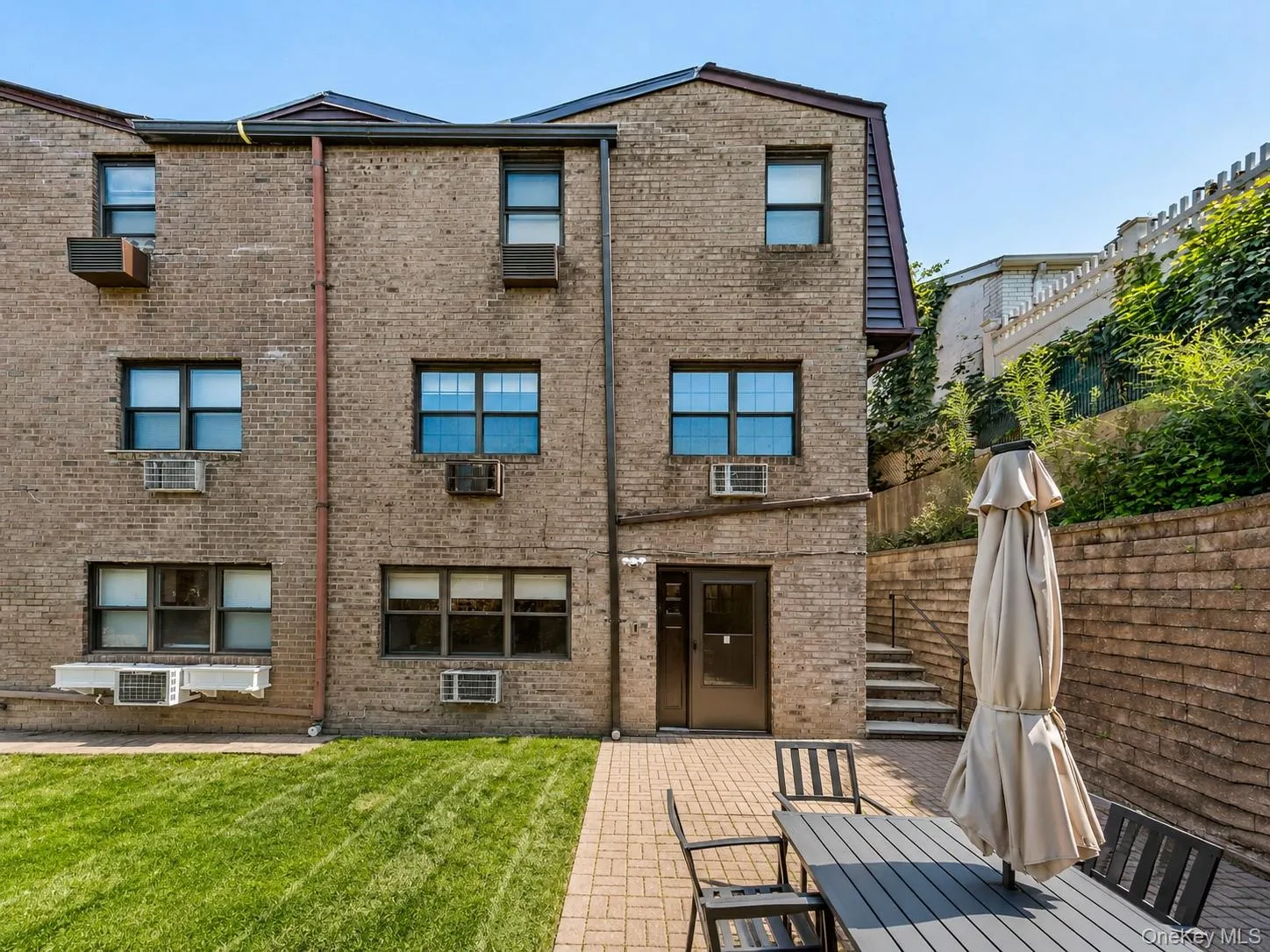 Brick exterior with multiple windows, leading to a paved patio area Brick exterior with multiple windows, leading to a paved patio area