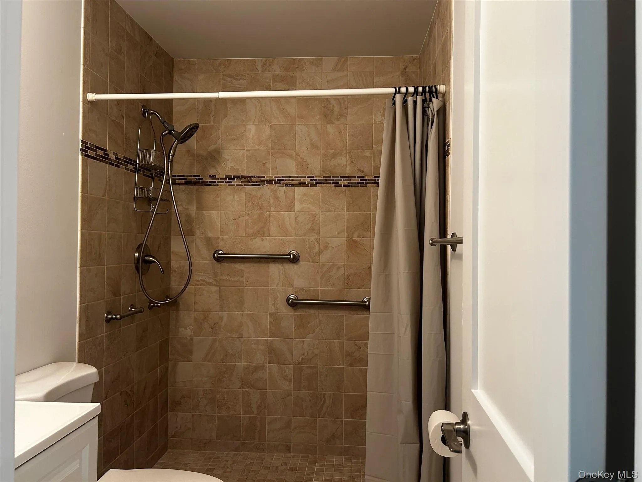 Tiled stall shower with decorative accent border, handheld shower fixture and grab bars Tiled stall shower with decorative accent border, handheld shower fixture and grab bars