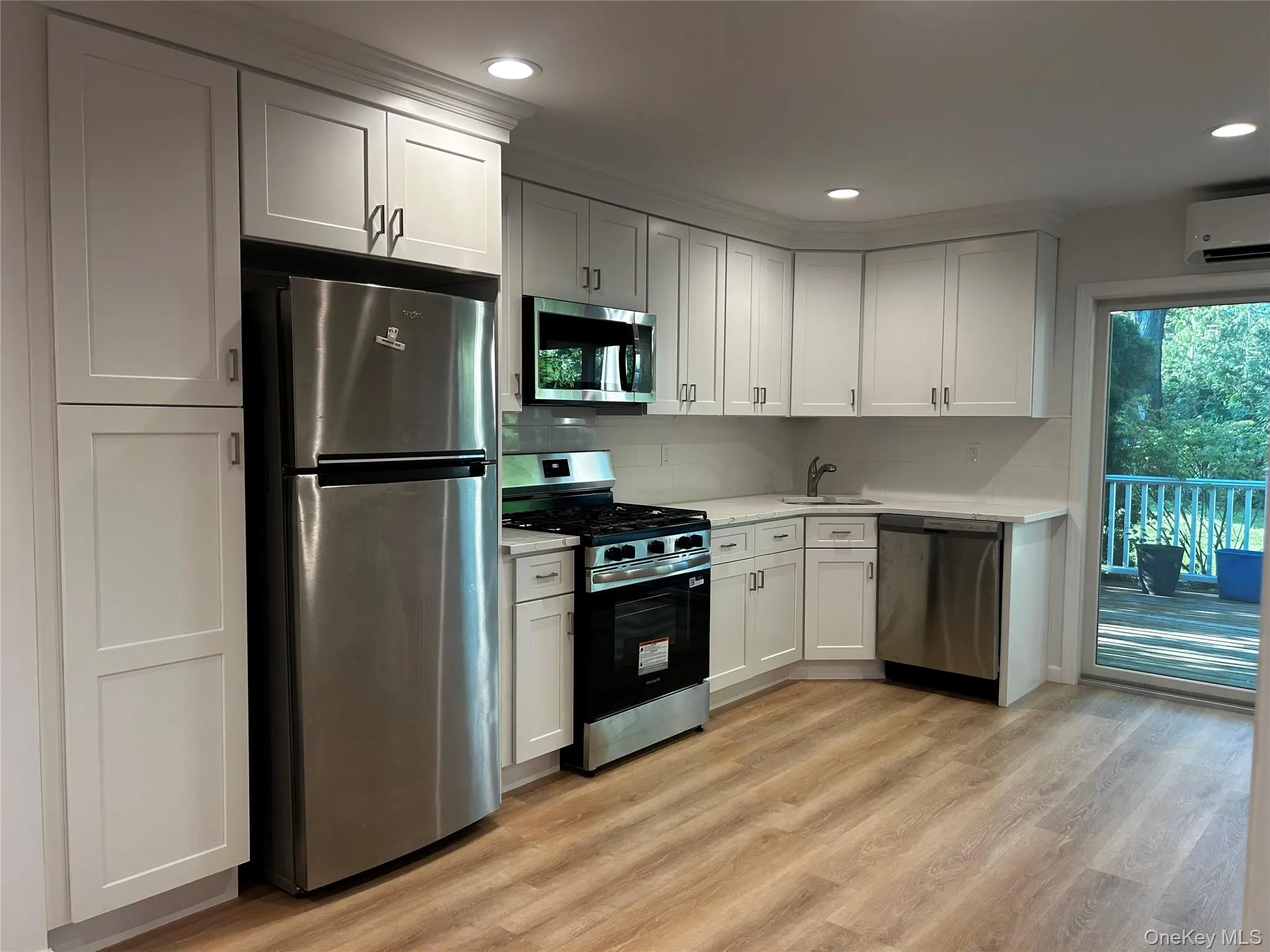 Modern kitchen featuring white shaker cabinetry, stainless steel appliances, luxury vinyl flooring, and direct access to an outdoor deck and the laundry area Modern kitchen featuring white shaker cabinetry, stainless steel appliances, luxury vinyl flooring, and direct access to an outdoor deck and the laundry area