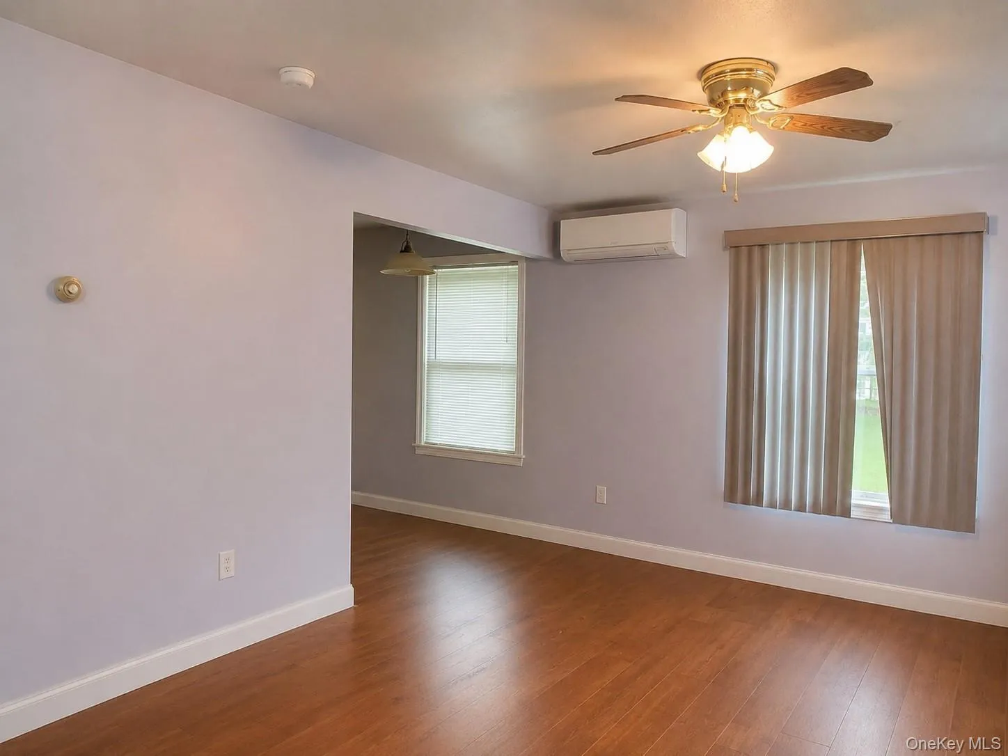 Spacious room showcasing warm wood-finish flooring, soft lavender walls, and abundant natural light from dual windows***Photos have been digitally staged to remove clutter*** Spacious room showcasing warm wood-finish flooring, soft lavender walls, and abundant natural light from dual windows***Photos have been digitally staged to remove clutter***