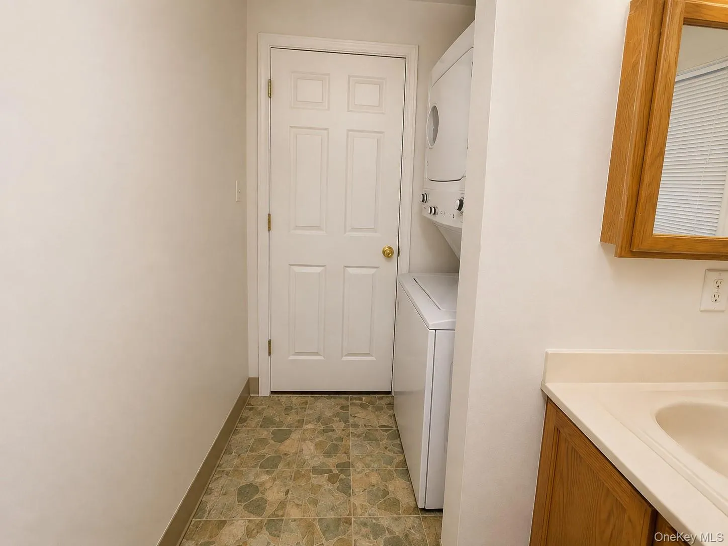 Dedicated laundry room featuring stackable washer and dryer units, tile flooring, and ample counter space with undermount sink and wood-finish cabinetry for convenient clothing care and storage***Photos have been digitally staged to remove clutter*** Dedicated laundry room featuring stackable washer and dryer units, tile flooring, and ample counter space with undermount sink and wood-finish cabinetry for convenient clothing care and storage***Photos have been digitally staged to remove clutter***