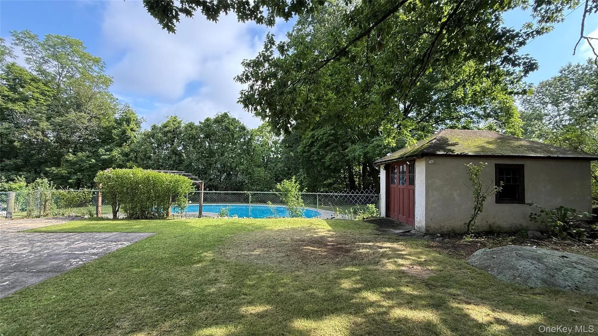 Fenced swimming pool, detached stucco structure, mature trees, green lawn, natural rock elements Fenced swimming pool, detached stucco structure, mature trees, green lawn, natural rock elements