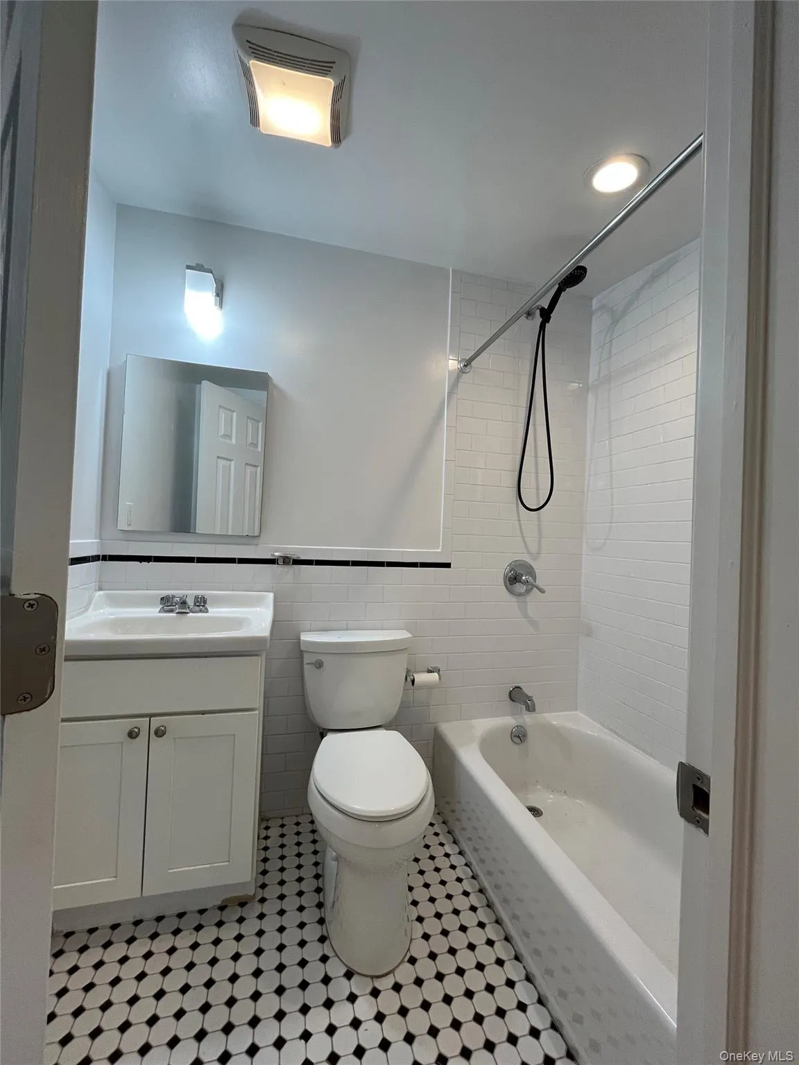 Black and white hexagonal floor tiling, subway tile shower surround, built-in bathtub, white vanity with integrated sink, and wall-mounted mirror Black and white hexagonal floor tiling, subway tile shower surround, built-in bathtub, white vanity with integrated sink, and wall-mounted mirror
