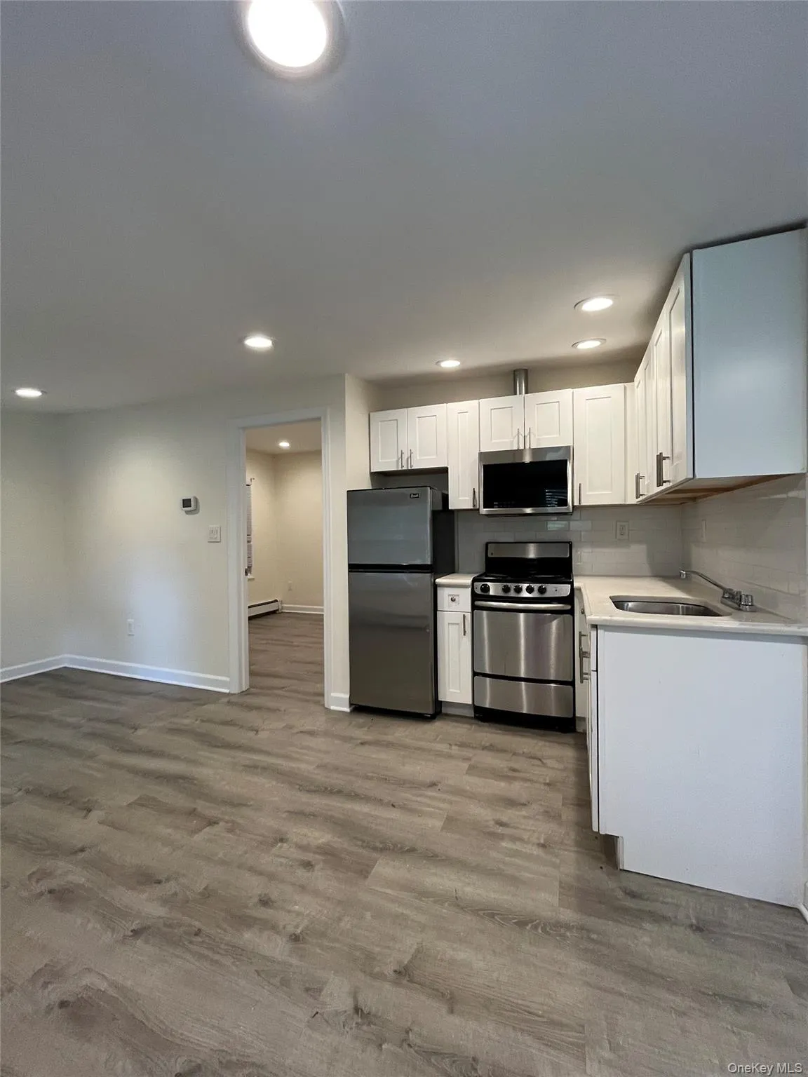 Kitchen featuring white cabinetry, stainless steel appliances, light-toned countertops, and wood-finish flooring Kitchen featuring white cabinetry, stainless steel appliances, light-toned countertops, and wood-finish flooring