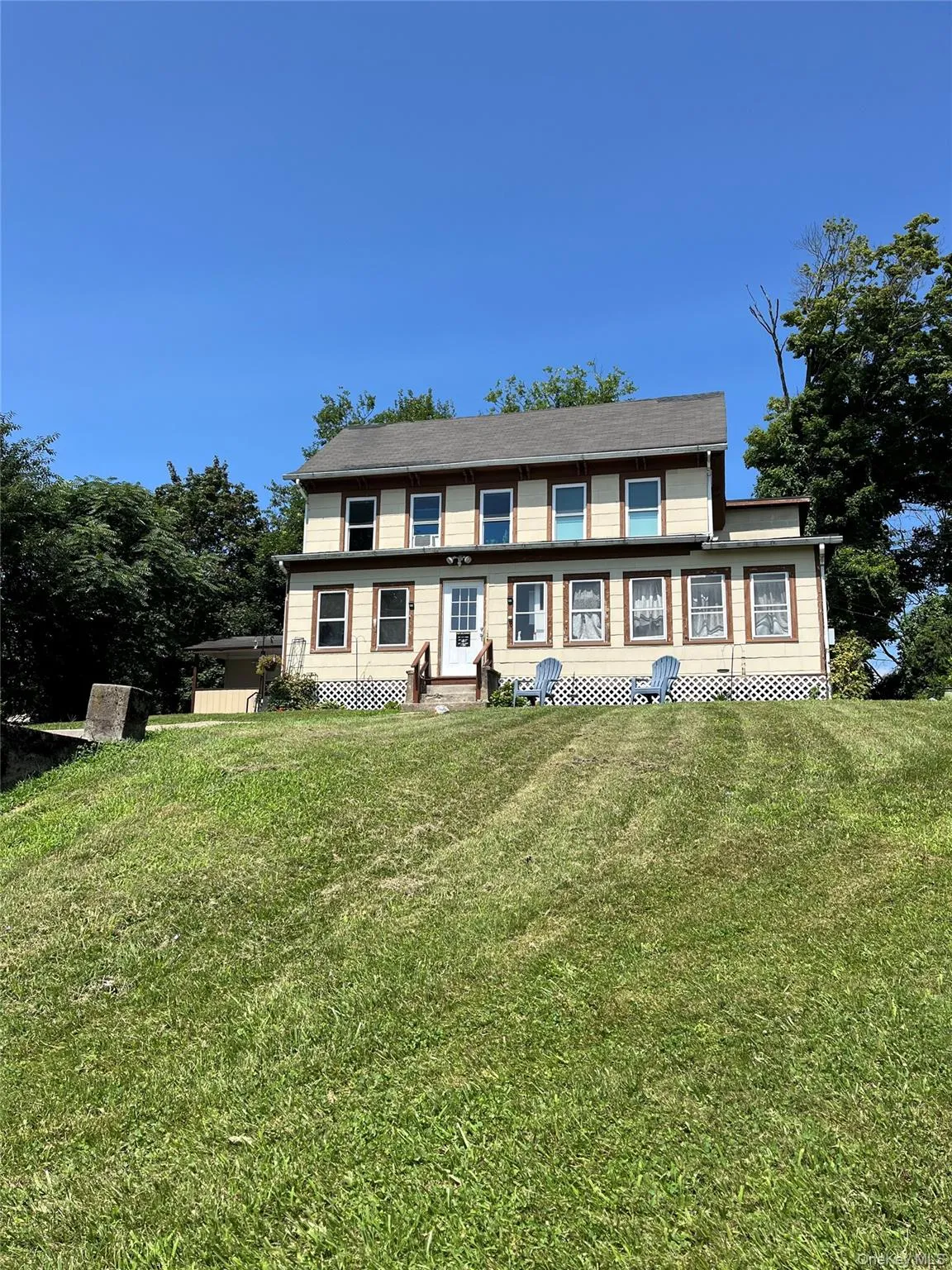 Two-story residence featuring a front entry door, multiple windows, and a sloped front lawn Two-story residence featuring a front entry door, multiple windows, and a sloped front lawn