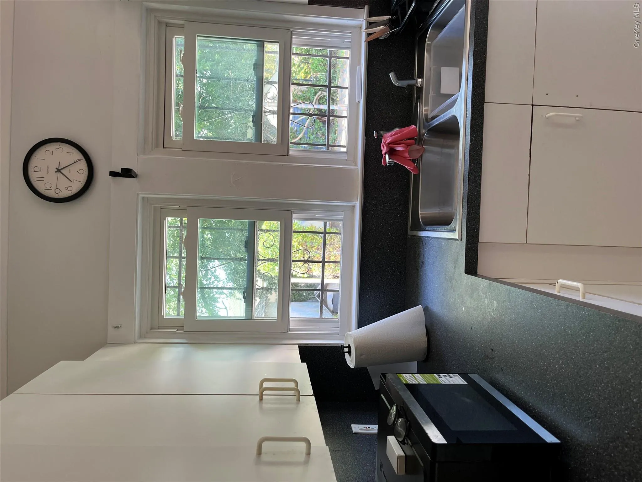 White upper cabinetry with contemporary hardware, two single-hung windows, dark speckled countertops, and a double-basin stainless steel sink White upper cabinetry with contemporary hardware, two single-hung windows, dark speckled countertops, and a double-basin stainless steel sink