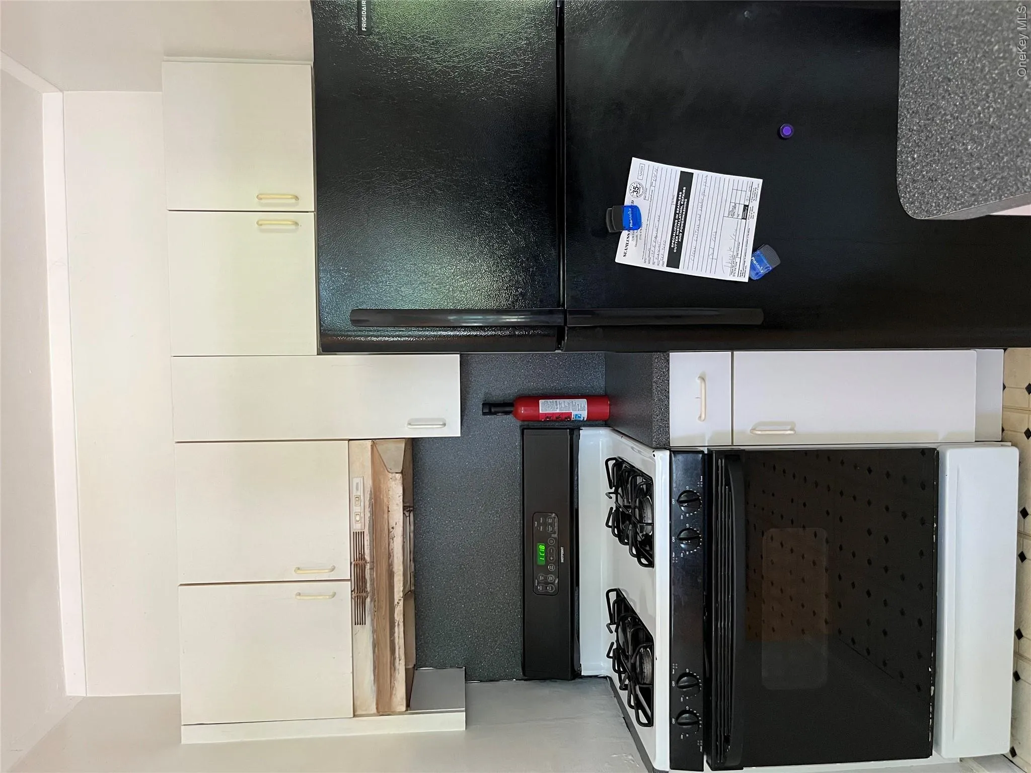 White upper cabinetry, black refrigerator, black and white range, and dark countertops White upper cabinetry, black refrigerator, black and white range, and dark countertops
