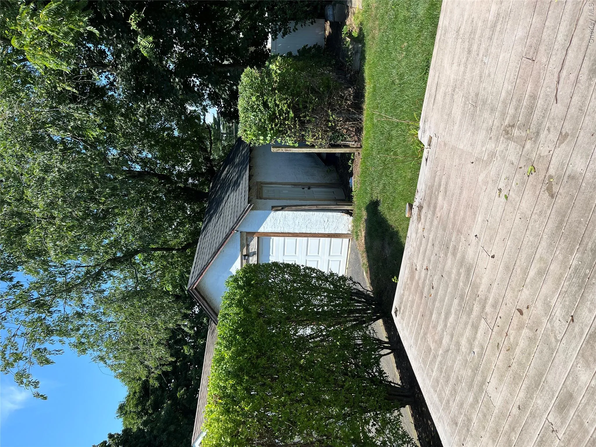 Expansive wood deck with surrounding mature hedges, a detached garage with an overhead door, and a separate shed structure Expansive wood deck with surrounding mature hedges, a detached garage with an overhead door, and a separate shed structure