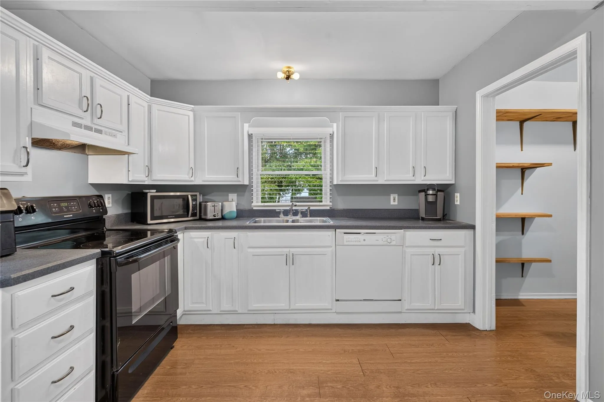 White cabinetry, dark countertops, black range, dishwasher, and wood-finish flooring White cabinetry, dark countertops, black range, dishwasher, and wood-finish flooring