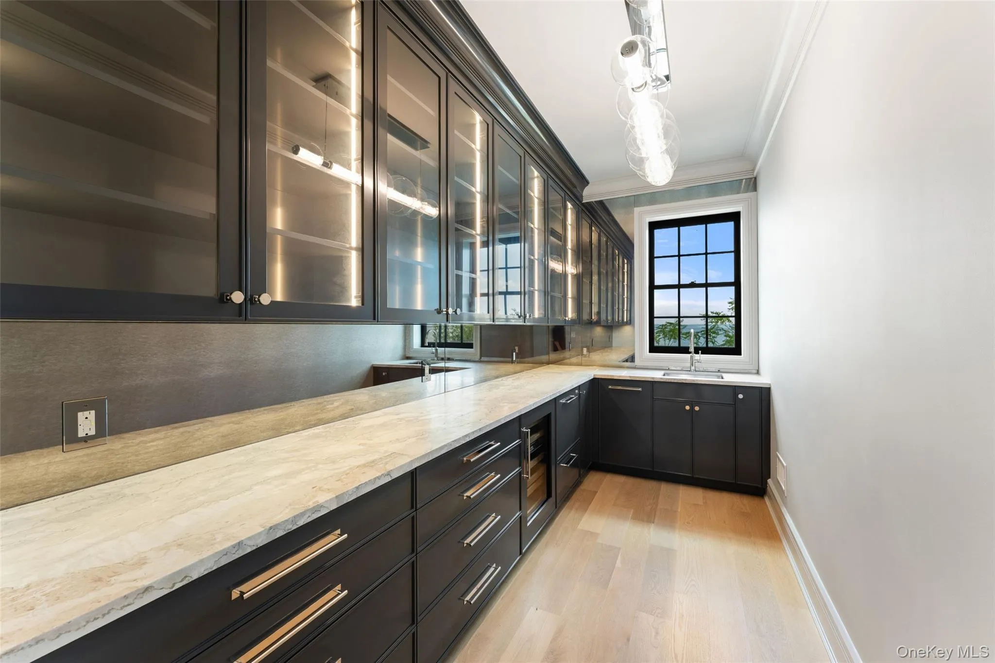 Sophisticated butler’s pantry with dark cabinetry, glass-front storage and stone counters. Sophisticated butler’s pantry with dark cabinetry, glass-front storage and stone counters.