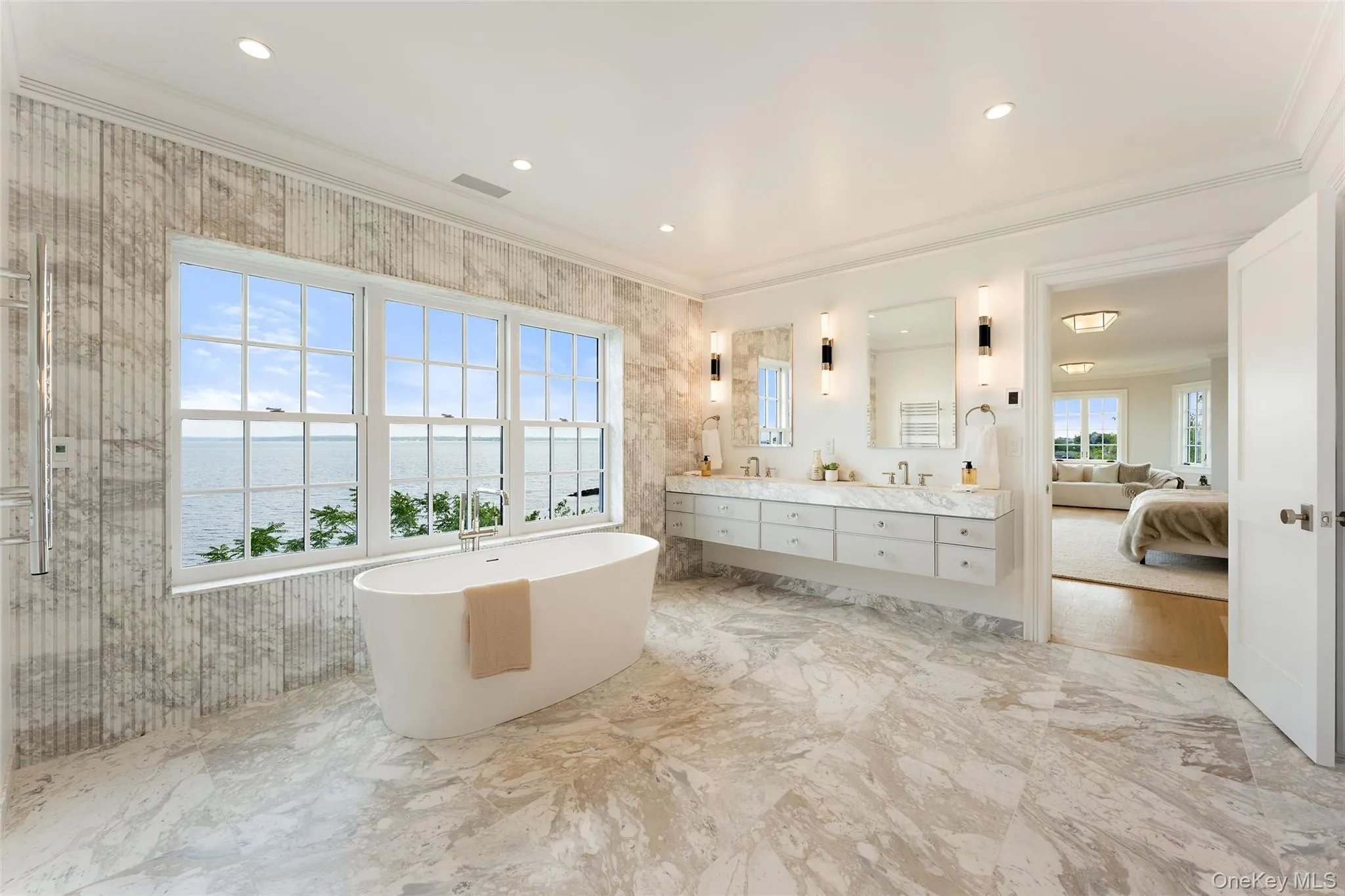 Luxurious primary bath with water views, expansive dual vanity, marble finishes and freestanding tub. Luxurious primary bath with water views, expansive dual vanity, marble finishes and freestanding tub.