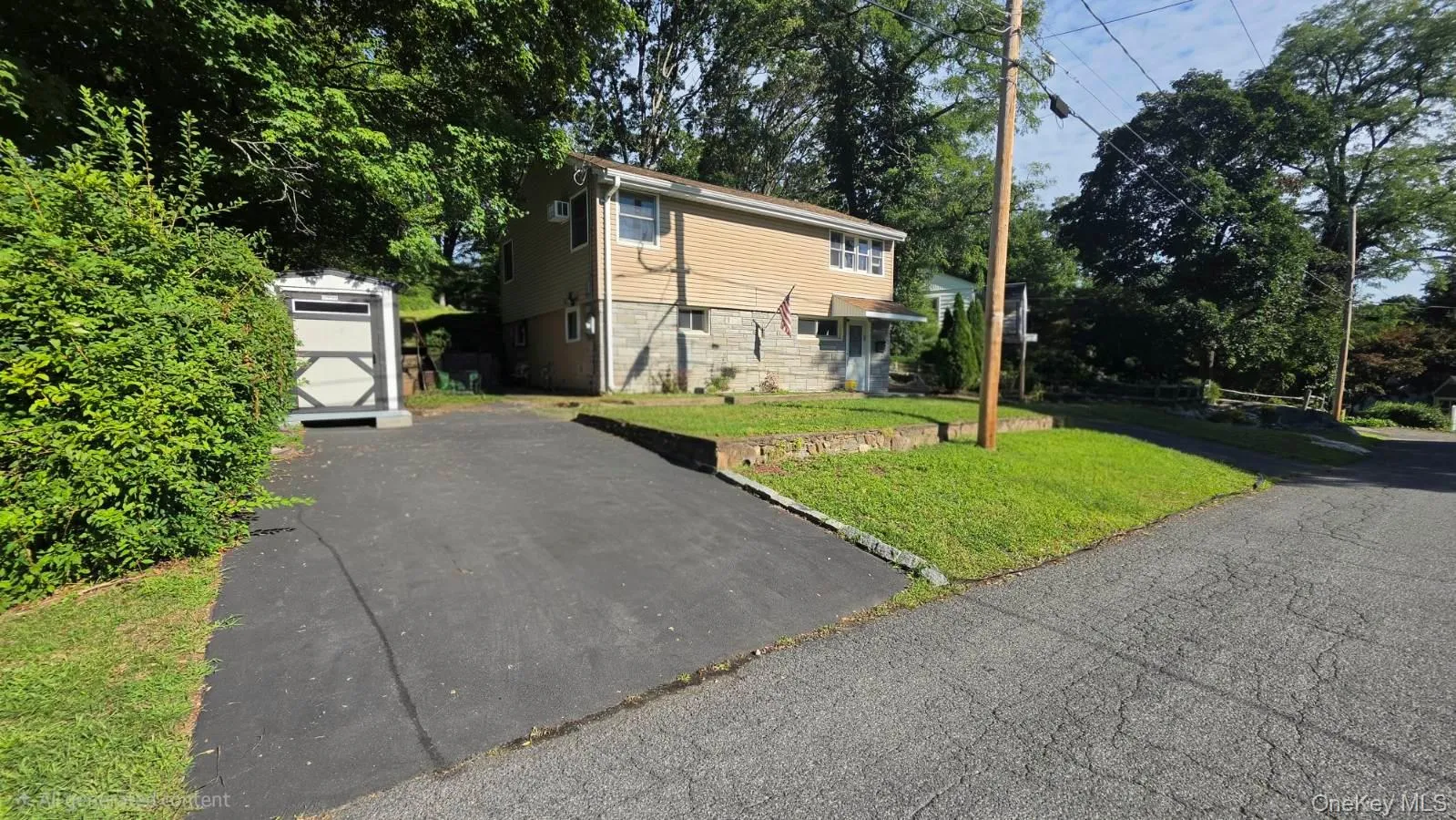 Split-level residence featuring a brick and stone facade, asphalt driveway, and a white storage shed Split-level residence featuring a brick and stone facade, asphalt driveway, and a white storage shed
