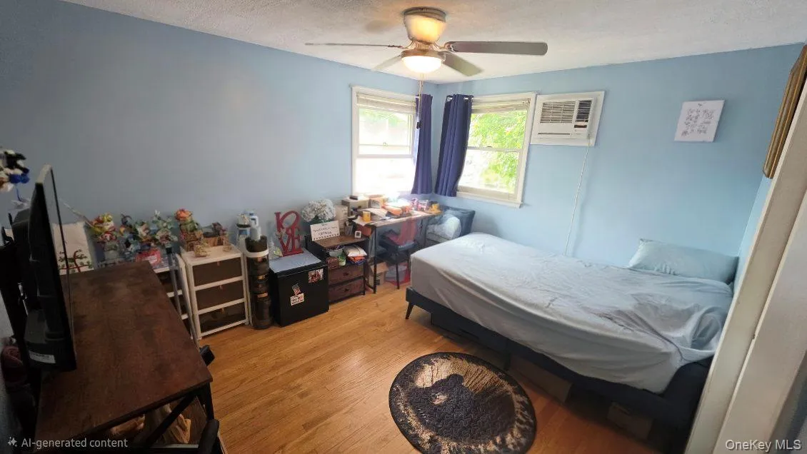 Hardwood flooring, painted walls, ceiling fan, multiple windows with natural light, and a wall-mounted air conditioning unit Hardwood flooring, painted walls, ceiling fan, multiple windows with natural light, and a wall-mounted air conditioning unit