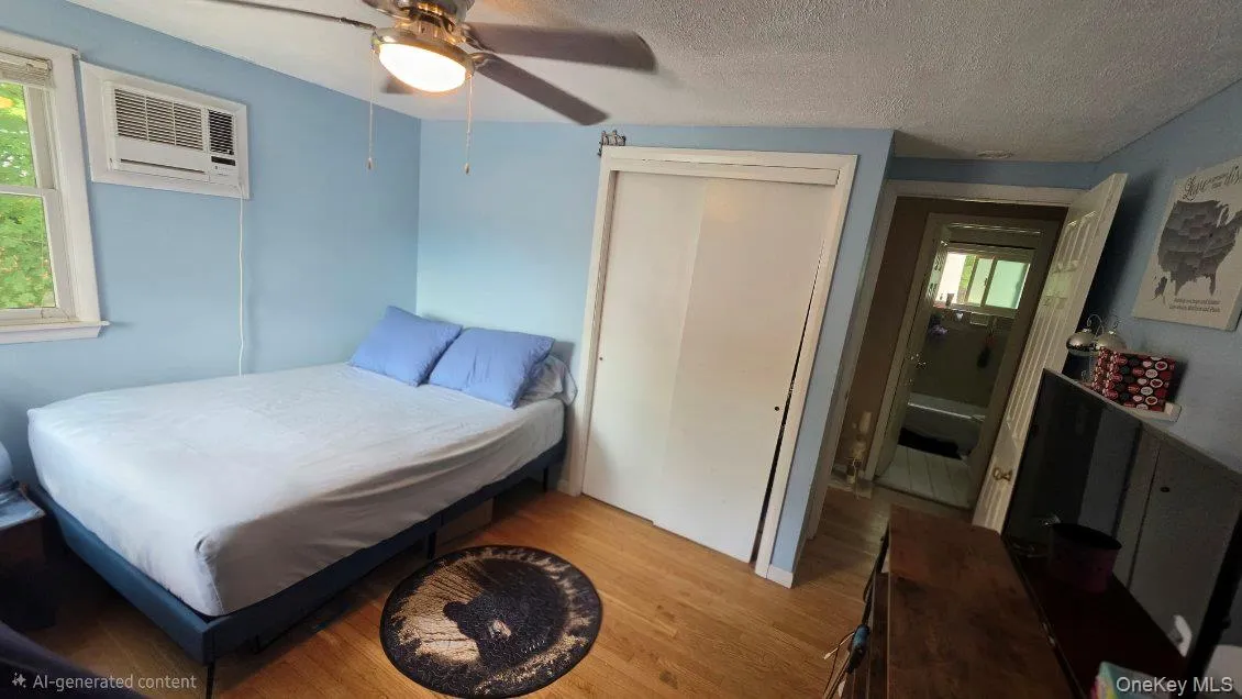 Wood-finish flooring, ceiling fan with integrated lighting, window-mounted air conditioning unit, and sliding closet doors Wood-finish flooring, ceiling fan with integrated lighting, window-mounted air conditioning unit, and sliding closet doors