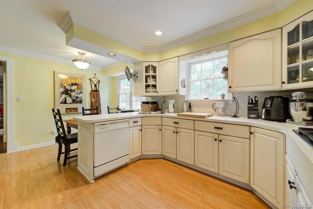 Kitchen featuring white dishwasher, a peninsula, a kitchen breakfast bar, glass insert cabinets, and backsplash Kitchen featuring white dishwasher, a peninsula, a kitchen breakfast bar, glass insert cabinets, and backsplash