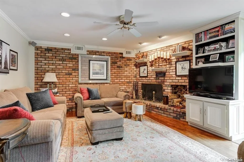 Living area featuring light wood-type flooring, crown molding, brick wall, a fireplace, and a ceiling fan Living area featuring light wood-type flooring, crown molding, brick wall, a fireplace, and a ceiling fan