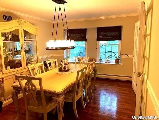 Dining area with a baseboard heating unit, dark wood-type flooring, and ornamental molding Dining area with a baseboard heating unit, dark wood-type flooring, and ornamental molding