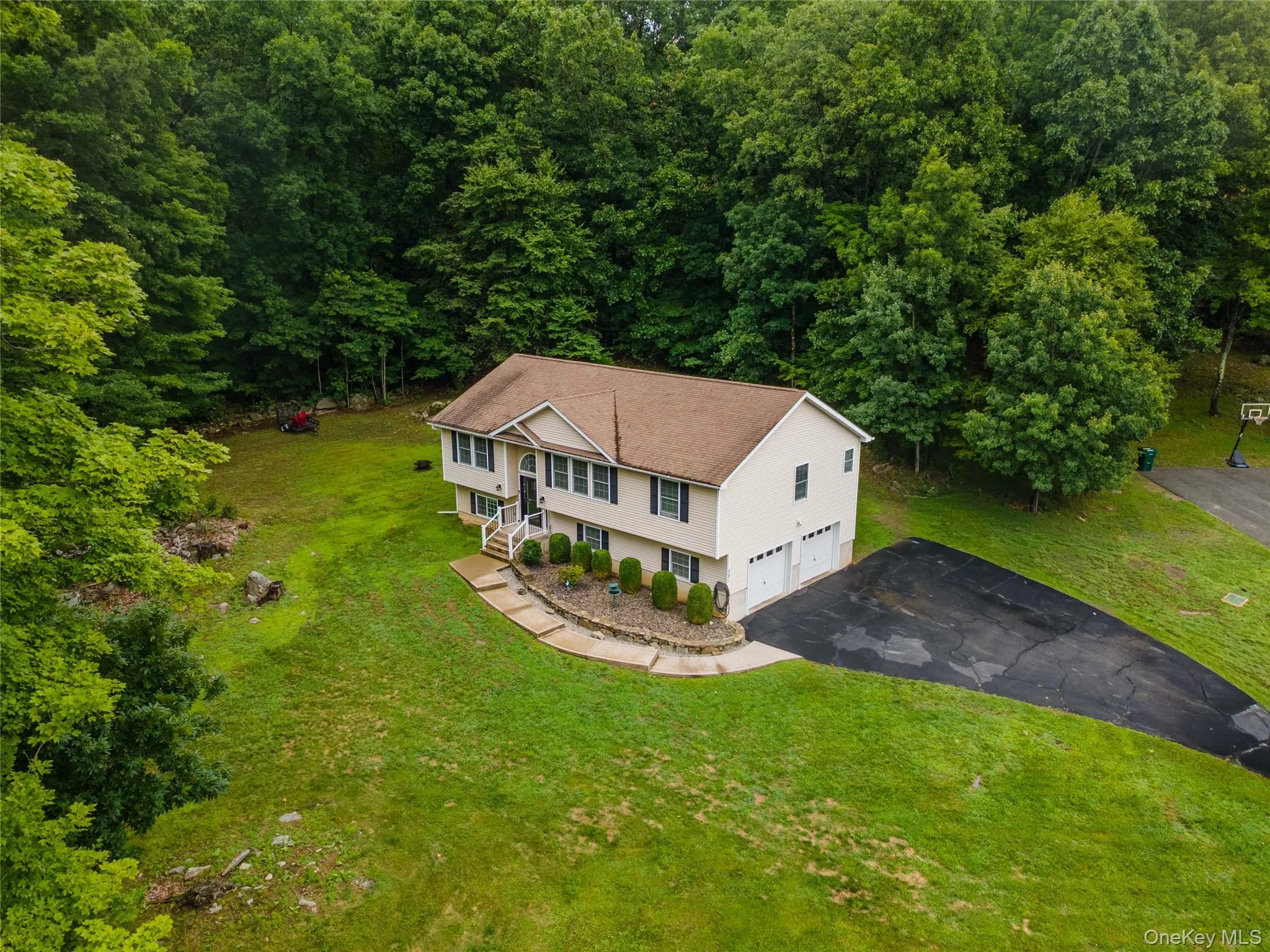 Split-level residence featuring a light-colored exterior, an attached two-car garage, and a paved driveway Split-level residence featuring a light-colored exterior, an attached two-car garage, and a paved driveway