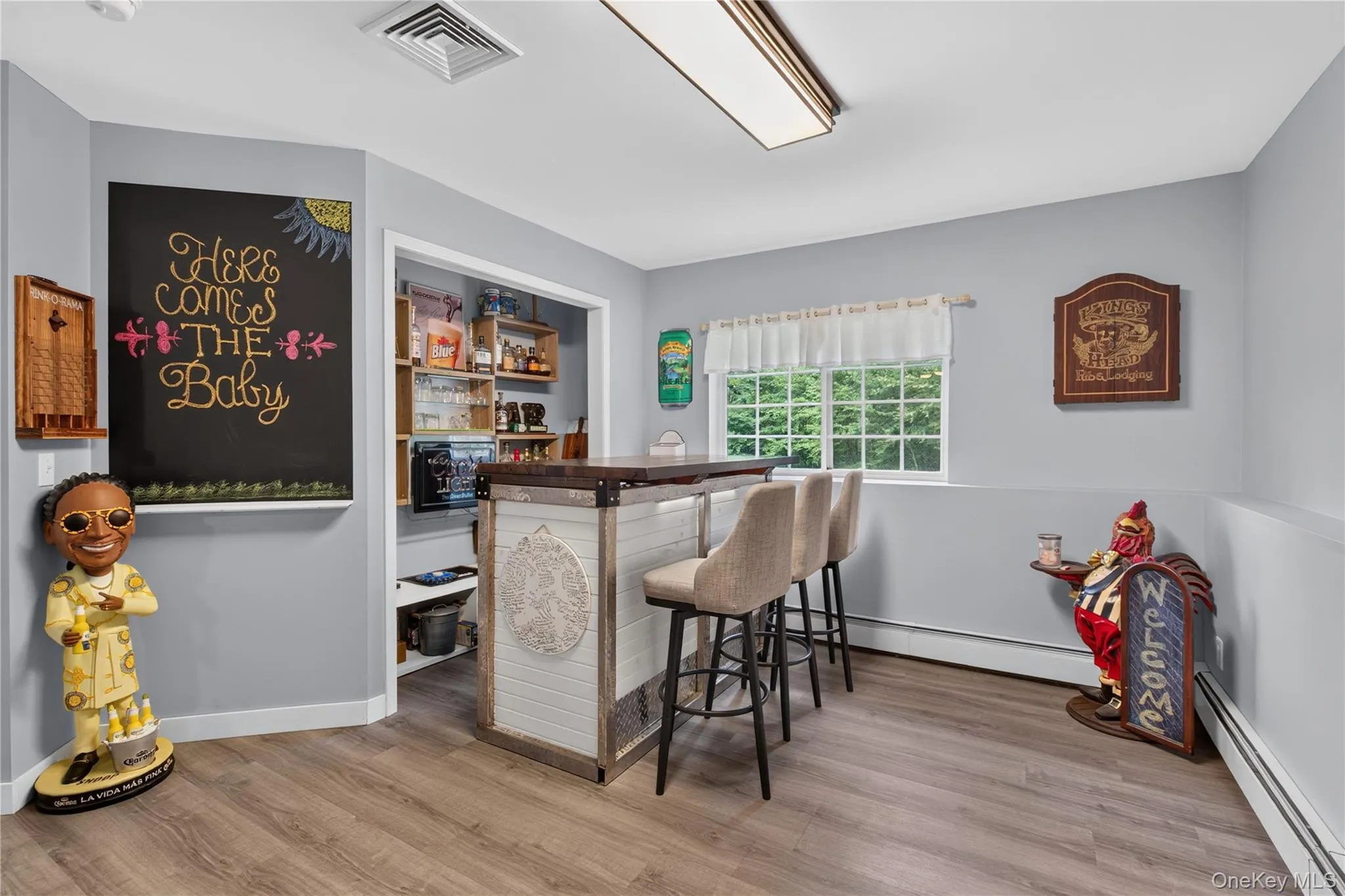 Built-in bar with seating, wood-finish flooring, recessed shelving, and a bright window Built-in bar with seating, wood-finish flooring, recessed shelving, and a bright window