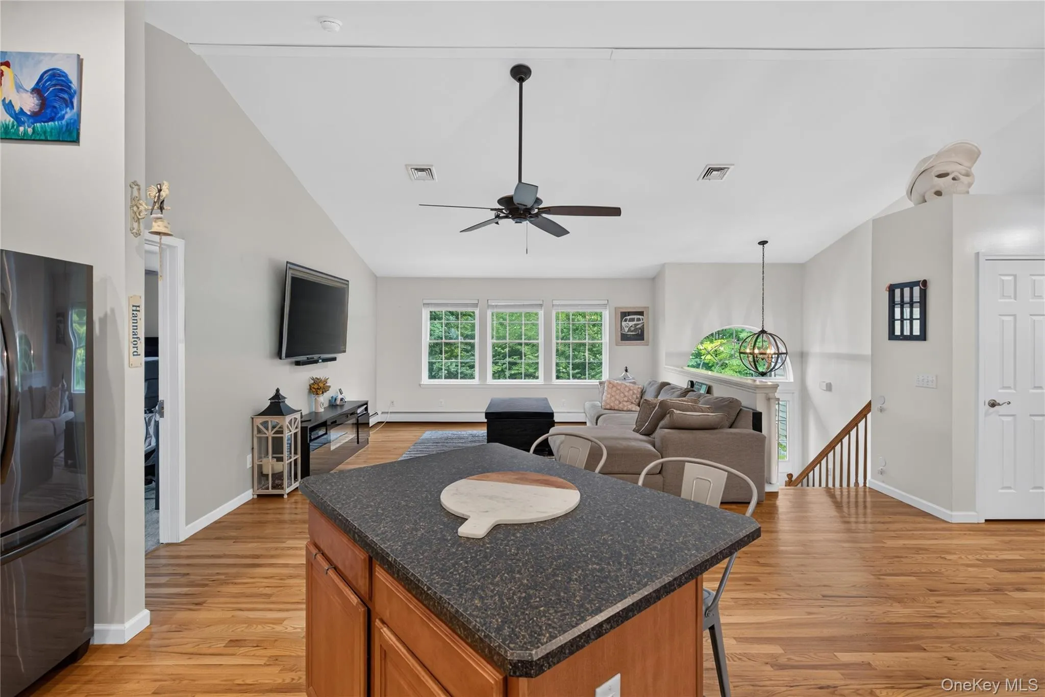 Wood-finish flooring throughout, vaulted ceiling, kitchen island with dark countertop, built-in refrigerator, and multiple large windows Wood-finish flooring throughout, vaulted ceiling, kitchen island with dark countertop, built-in refrigerator, and multiple large windows