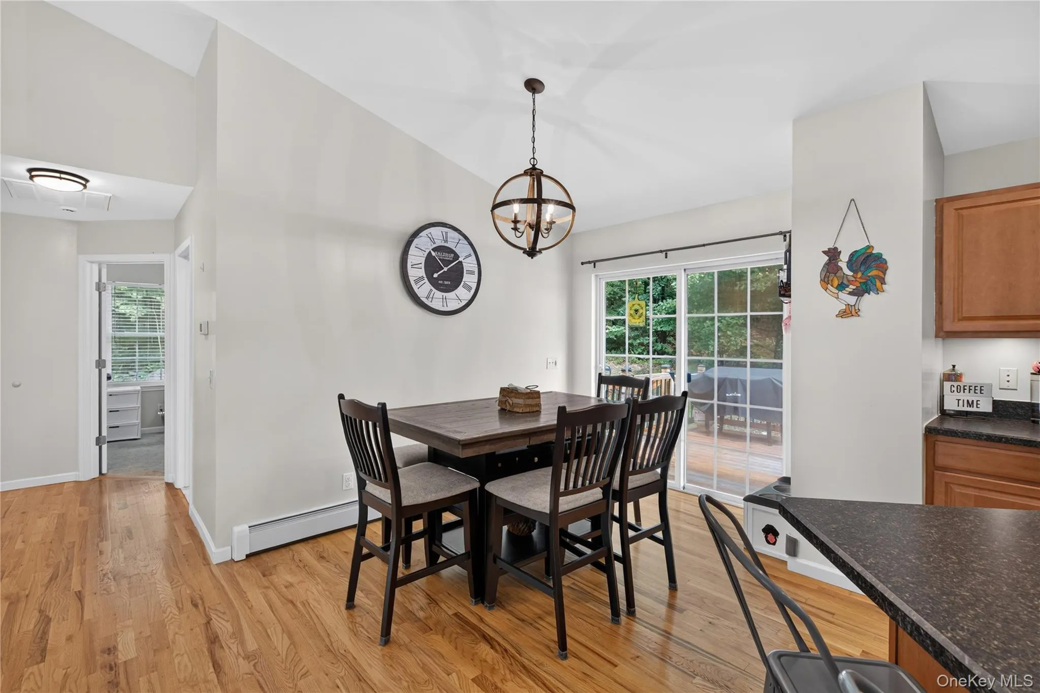 Open-concept area featuring hardwood flooring, a vaulted ceiling, a spherical pendant light fixture, a sliding glass door, and a built-in kitchen countertop Open-concept area featuring hardwood flooring, a vaulted ceiling, a spherical pendant light fixture, a sliding glass door, and a built-in kitchen countertop