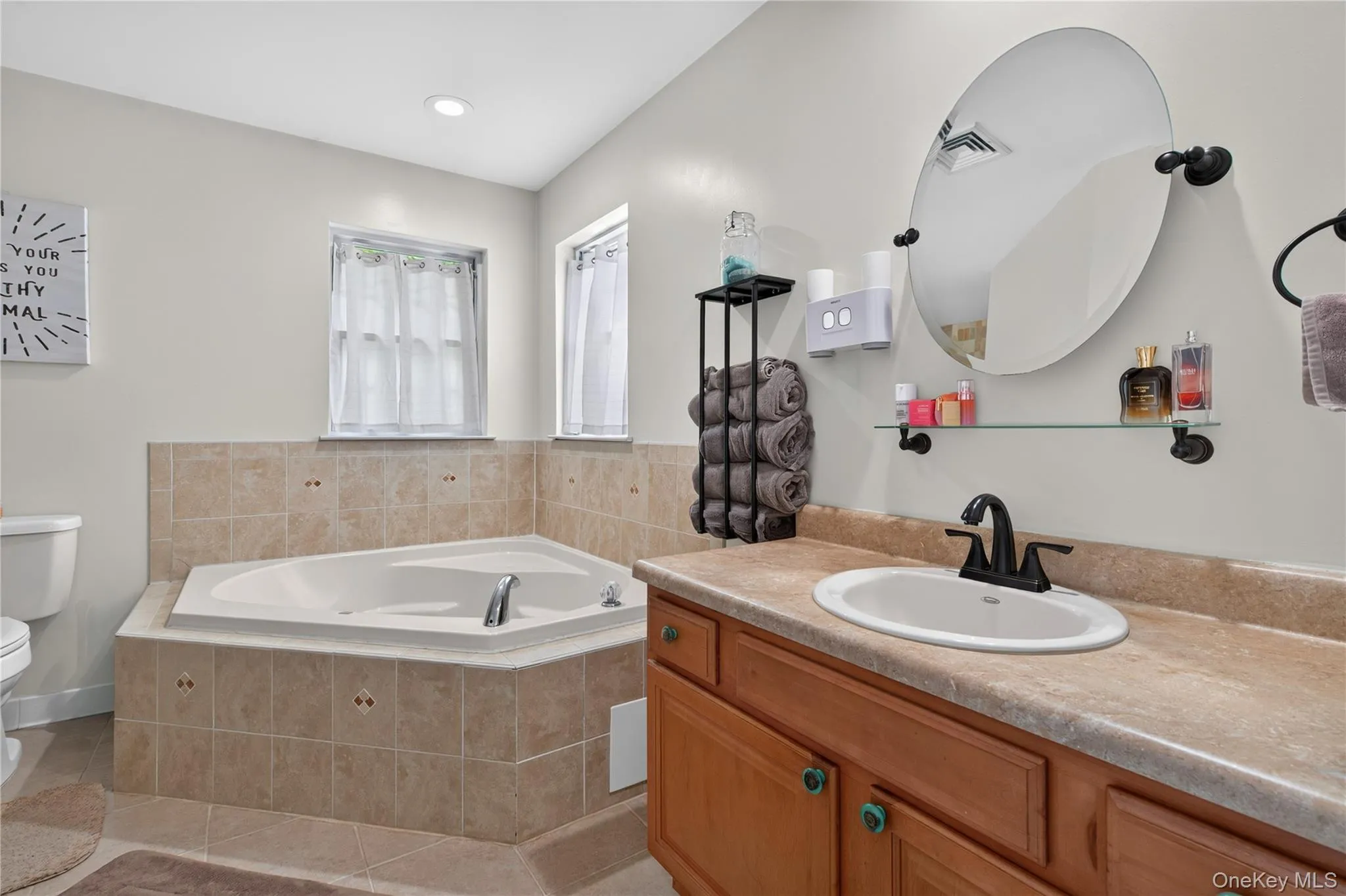 Corner soaking tub with tiled surround, wood-finish vanity with an undermount sink, and an oval vanity mirror Corner soaking tub with tiled surround, wood-finish vanity with an undermount sink, and an oval vanity mirror