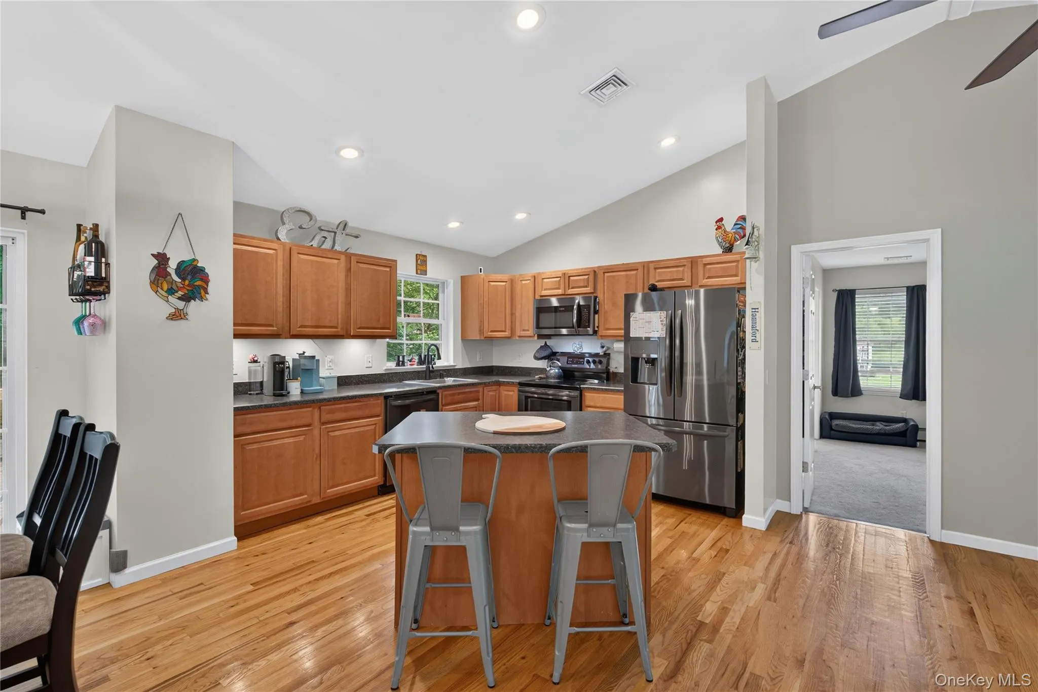 Kitchen featuring wood-finish flooring, recessed lighting, wood cabinetry, stainless steel appliances, and a central island with seating Kitchen featuring wood-finish flooring, recessed lighting, wood cabinetry, stainless steel appliances, and a central island with seating