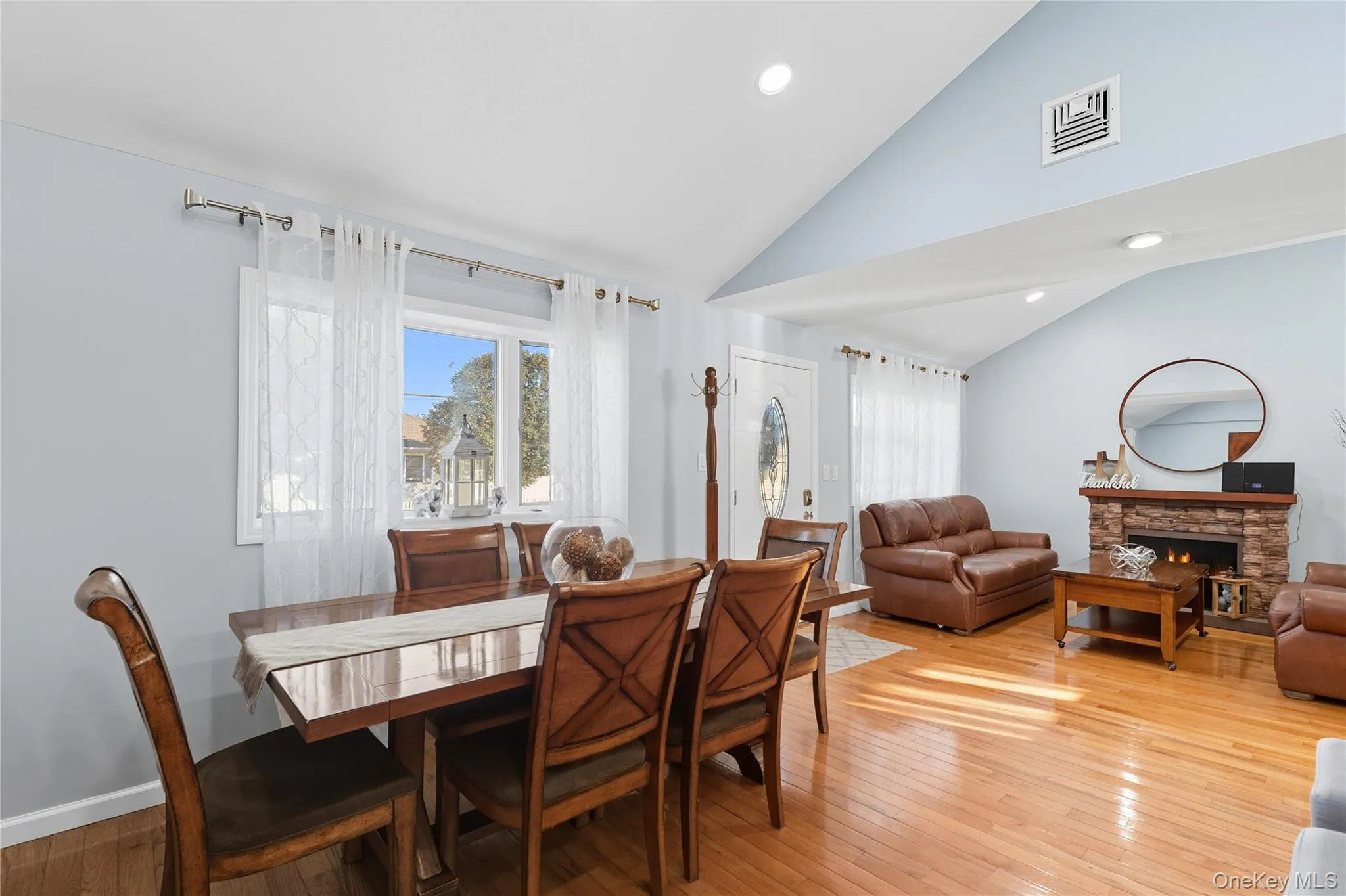 Dining area featuring light wood-type flooring, healthy amount of natural light, a stone fireplace, recessed lighting, and high vaulted ceiling Dining area featuring light wood-type flooring, healthy amount of natural light, a stone fireplace, recessed lighting, and high vaulted ceiling