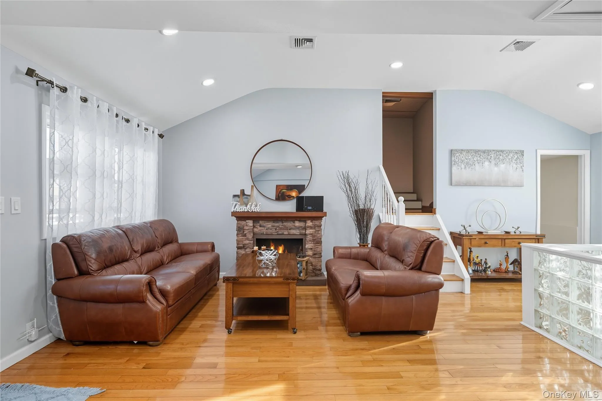 Living area featuring recessed lighting, lofted ceiling, a fireplace, light wood finished floors, and stairway Living area featuring recessed lighting, lofted ceiling, a fireplace, light wood finished floors, and stairway