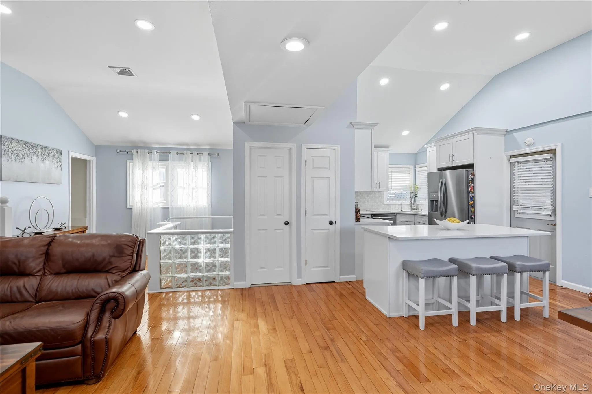 Kitchen featuring vaulted ceiling, a kitchen breakfast bar, white cabinetry, open floor plan, and light wood-type flooring Kitchen featuring vaulted ceiling, a kitchen breakfast bar, white cabinetry, open floor plan, and light wood-type flooring
