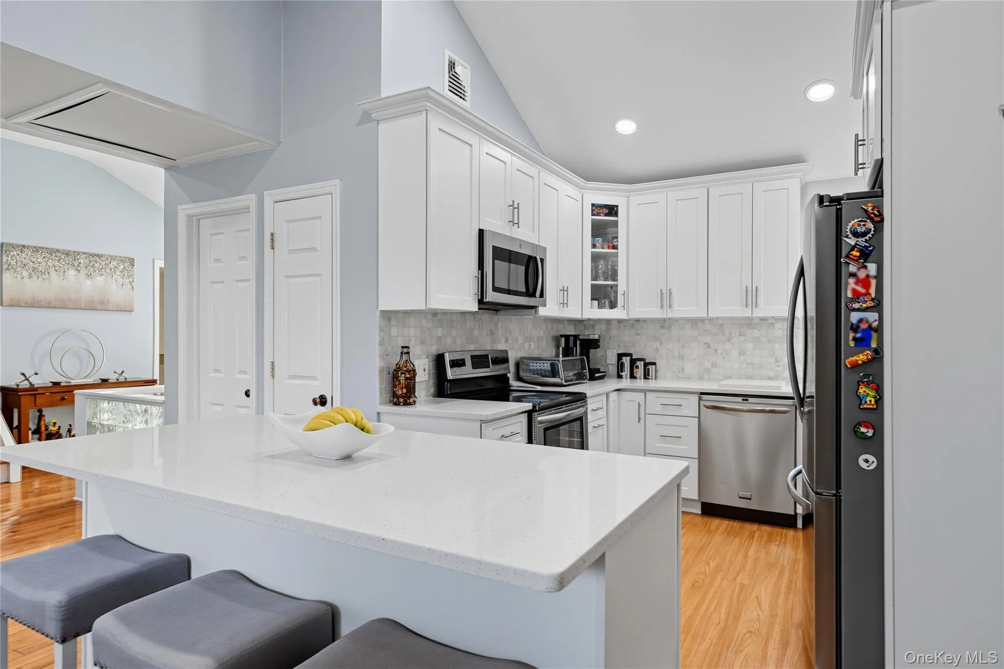 Kitchen featuring lofted ceiling, glass insert cabinets, stainless steel appliances, white cabinets, and light stone counters Kitchen featuring lofted ceiling, glass insert cabinets, stainless steel appliances, white cabinets, and light stone counters