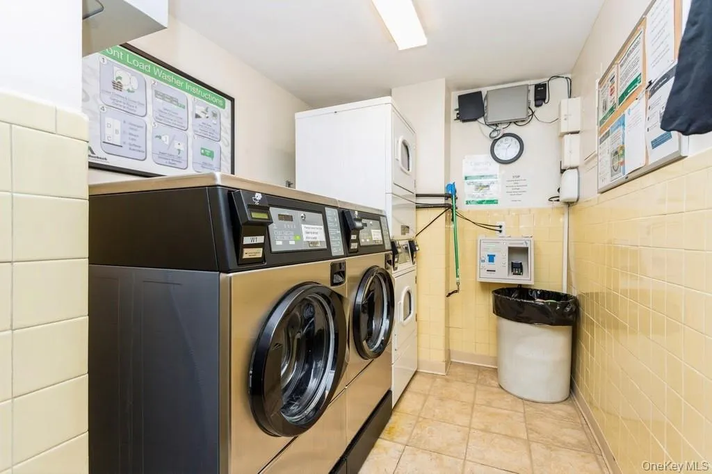 Shared laundry area featuring independent washer and dryer, a wainscoted wall, light tile patterned floors, and tile walls Shared laundry area featuring independent washer and dryer, a wainscoted wall, light tile patterned floors, and tile walls