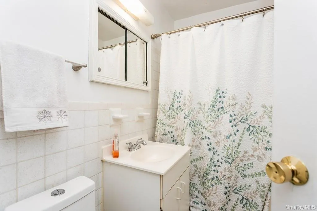 Full bath featuring toilet, vanity, a wainscoted wall, and tile walls Full bath featuring toilet, vanity, a wainscoted wall, and tile walls