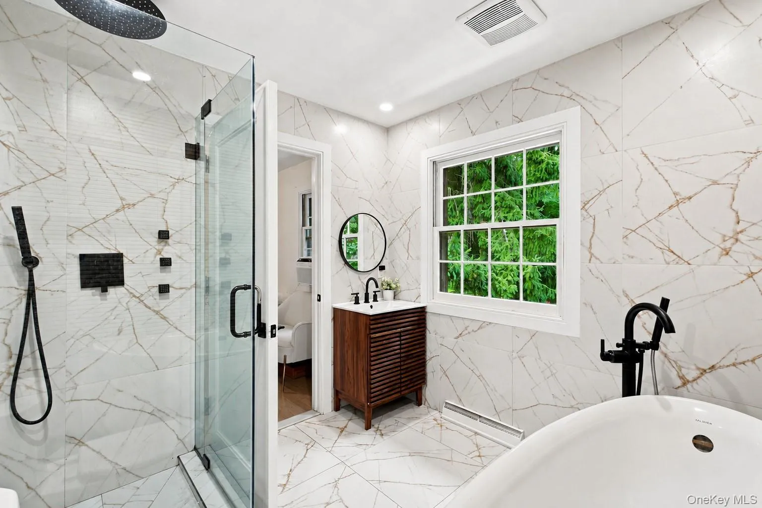 Glass-enclosed shower with matte black fixtures, freestanding soaking tub, and a window for natural illumination Glass-enclosed shower with matte black fixtures, freestanding soaking tub, and a window for natural illumination
