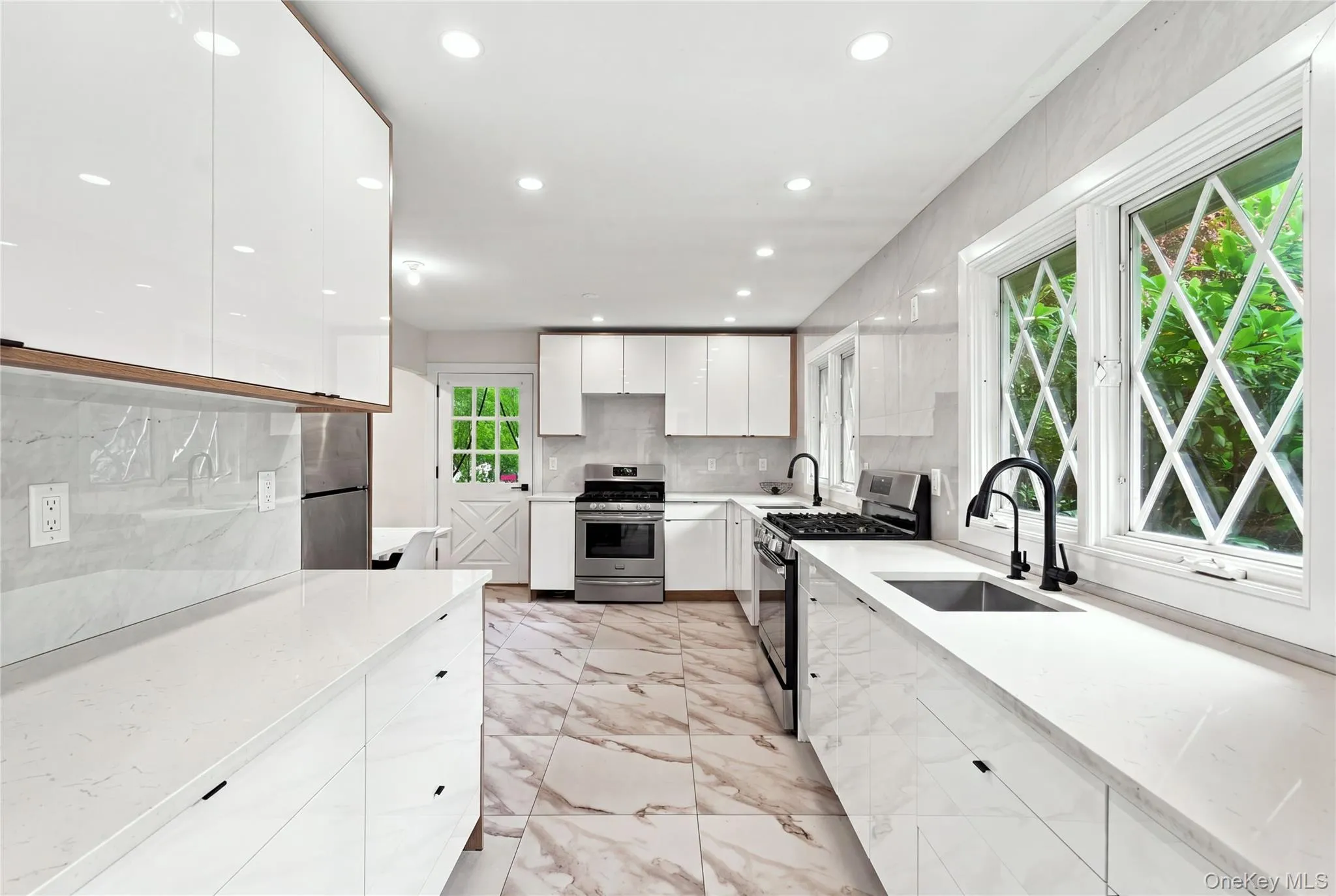 Kitchen featuring white flat-panel cabinetry, white countertops, stainless steel appliances, black fixtures, and patterned flooring Kitchen featuring white flat-panel cabinetry, white countertops, stainless steel appliances, black fixtures, and patterned flooring