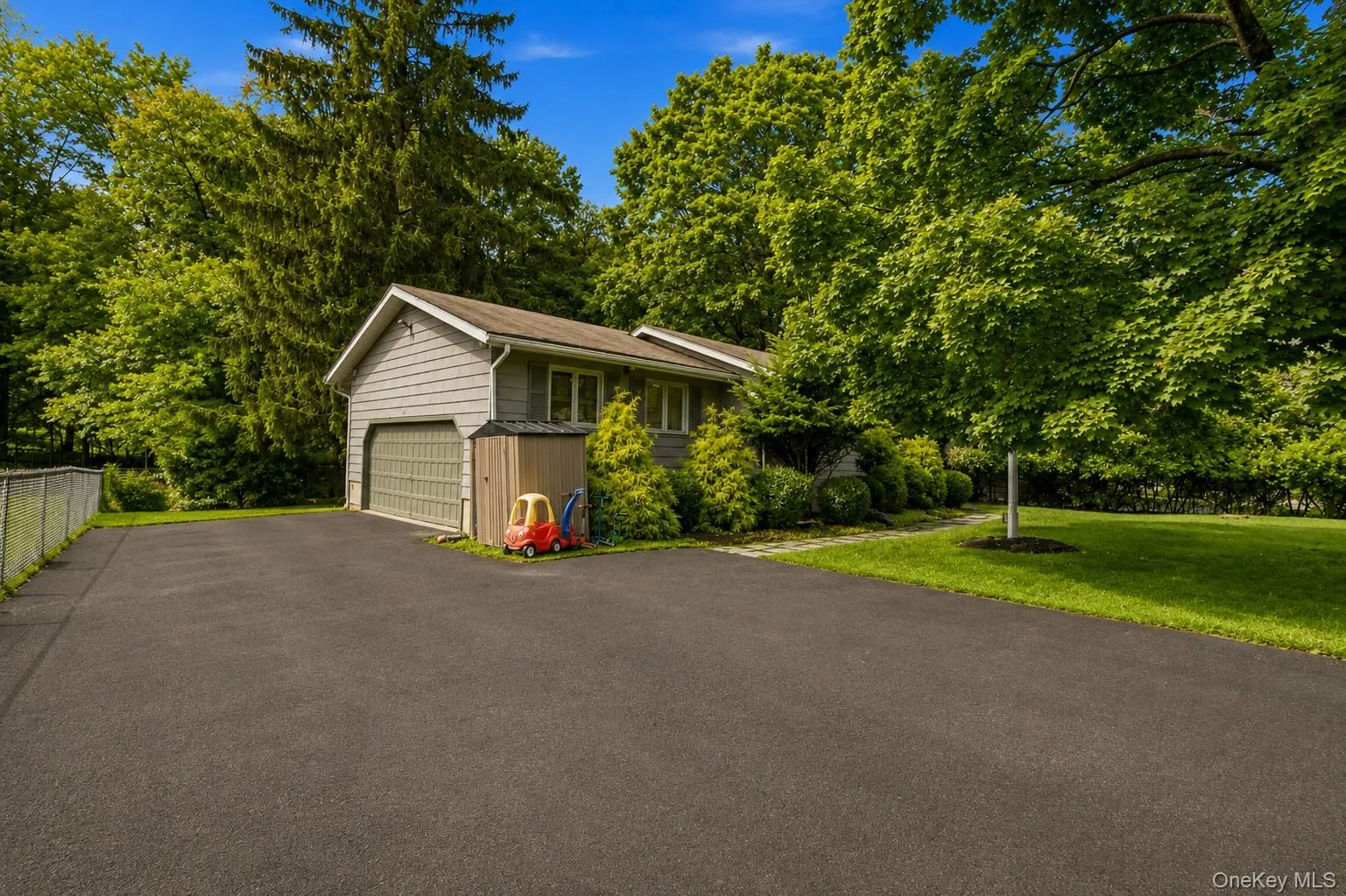 Siding exterior with an attached garage, paved driveway, and manicured lawn surrounded by mature trees Siding exterior with an attached garage, paved driveway, and manicured lawn surrounded by mature trees