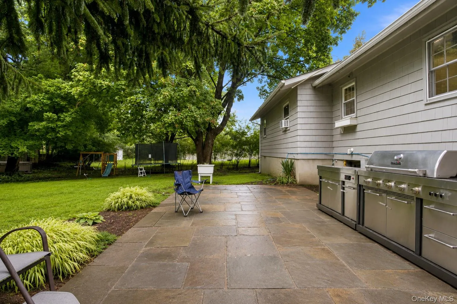 Expansive patio with stone pavers and a built-in outdoor kitchen featuring stainless steel appliances Expansive patio with stone pavers and a built-in outdoor kitchen featuring stainless steel appliances