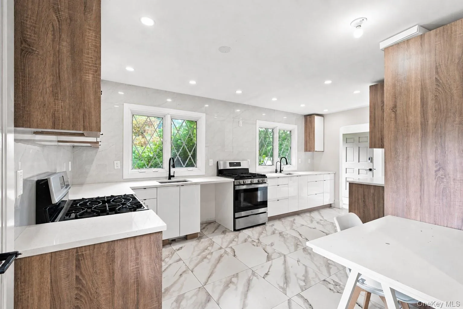 Contemporary kitchen featuring wood-finish cabinetry, white slab cabinet fronts, white countertops, and a full tile backsplash Contemporary kitchen featuring wood-finish cabinetry, white slab cabinet fronts, white countertops, and a full tile backsplash