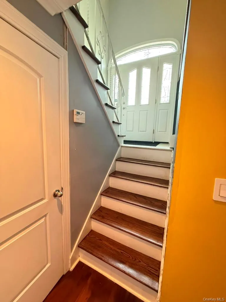 Entryway featuring a wood-finish staircase with white risers, a white paneled door, and a decorative transom window above the main entry Entryway featuring a wood-finish staircase with white risers, a white paneled door, and a decorative transom window above the main entry