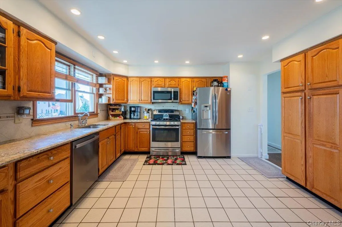 Kitchen featuring backsplash, sink, light tile patterned floors, light stone counters, and stainless steel appliances Kitchen featuring backsplash, sink, light tile patterned floors, light stone counters, and stainless steel appliances