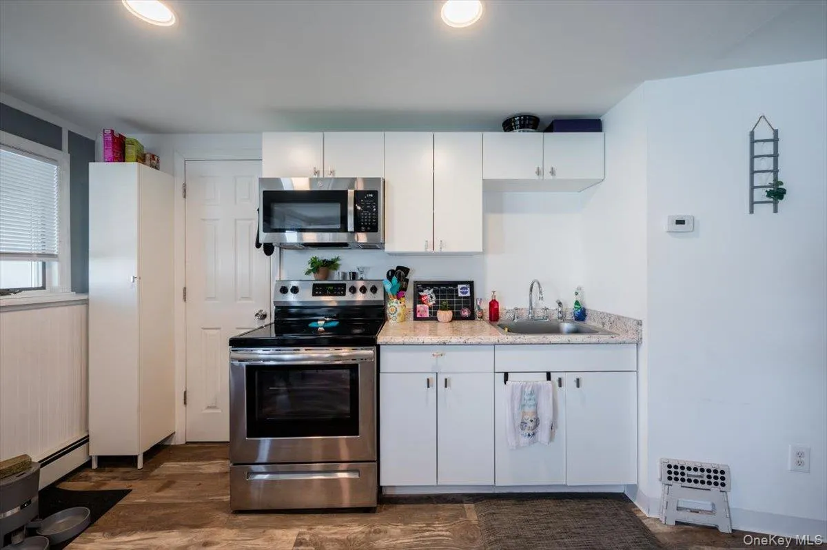 Kitchen featuring appliances with stainless steel finishes, dark wood-type flooring, sink, a baseboard radiator, and white cabinets Kitchen featuring appliances with stainless steel finishes, dark wood-type flooring, sink, a baseboard radiator, and white cabinets