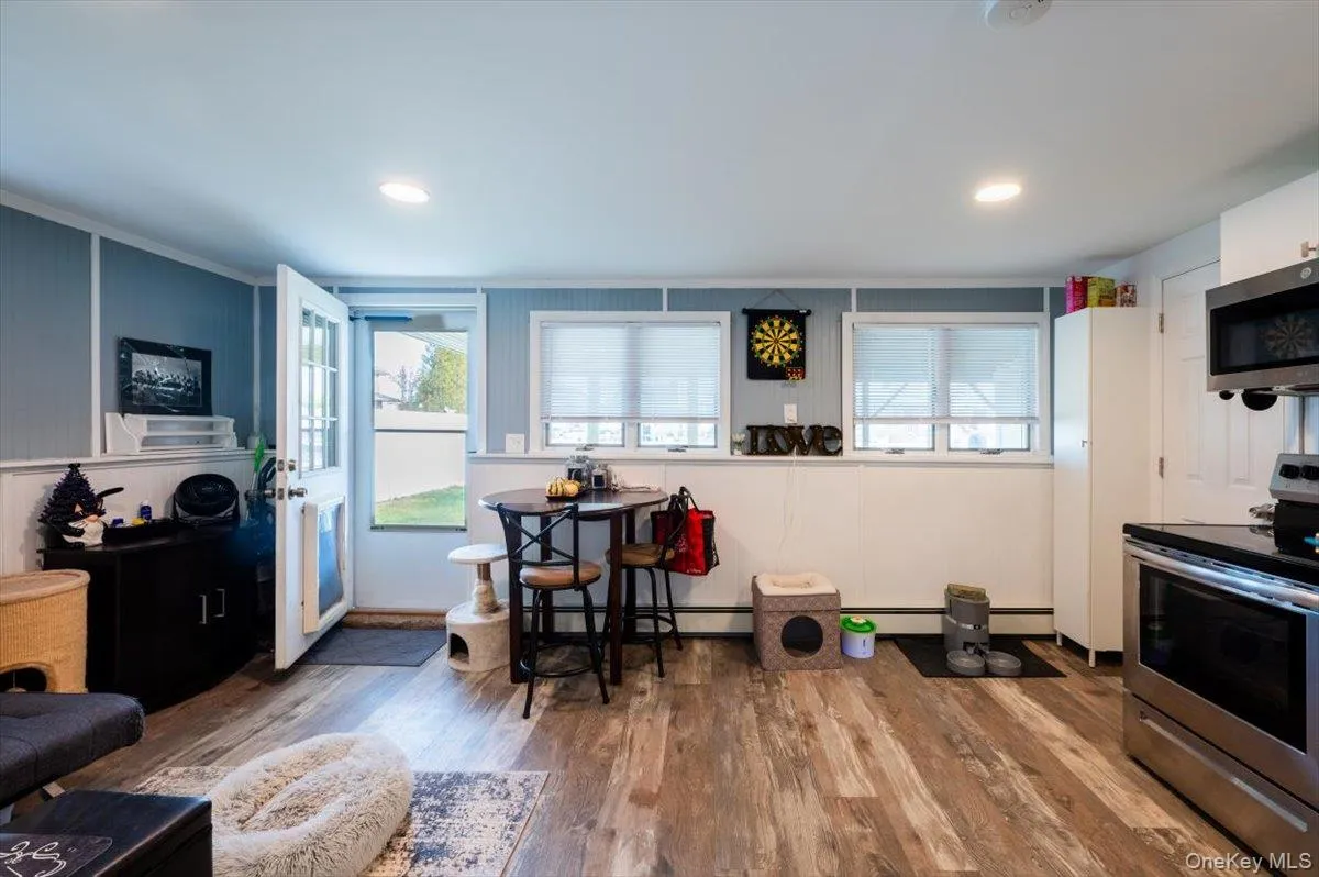 Kitchen featuring baseboard heating, hardwood / wood-style flooring, white cabinets, and appliances with stainless steel finishes Kitchen featuring baseboard heating, hardwood / wood-style flooring, white cabinets, and appliances with stainless steel finishes