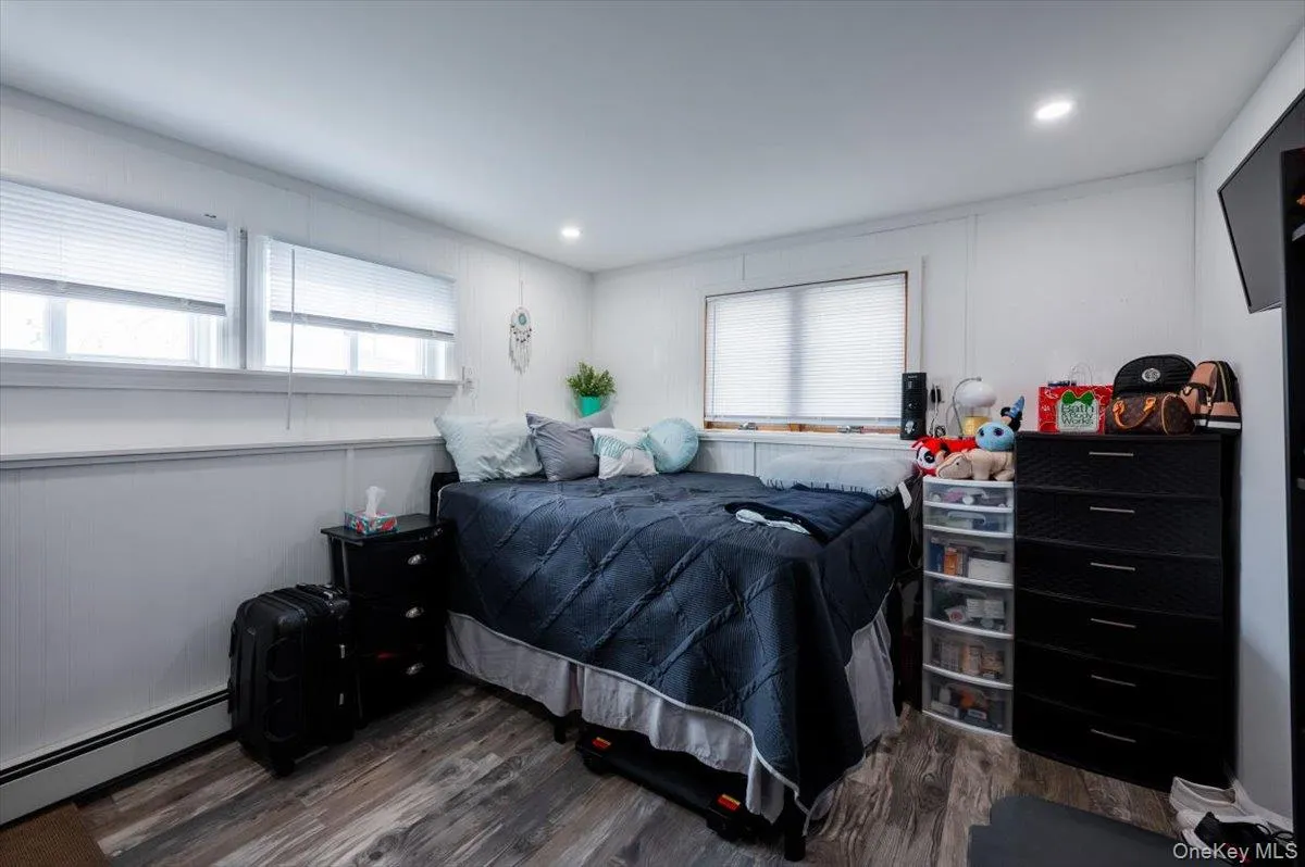 Bedroom with a baseboard radiator, multiple windows, and dark wood-type flooring Bedroom with a baseboard radiator, multiple windows, and dark wood-type flooring