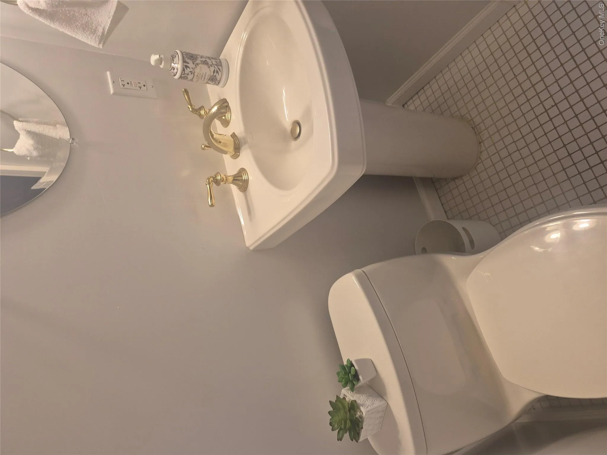 Powder Room with Pedestal sink with brass-finish faucet, white square tile flooring, and a round wall mirror Powder Room with Pedestal sink with brass-finish faucet, white square tile flooring, and a round wall mirror