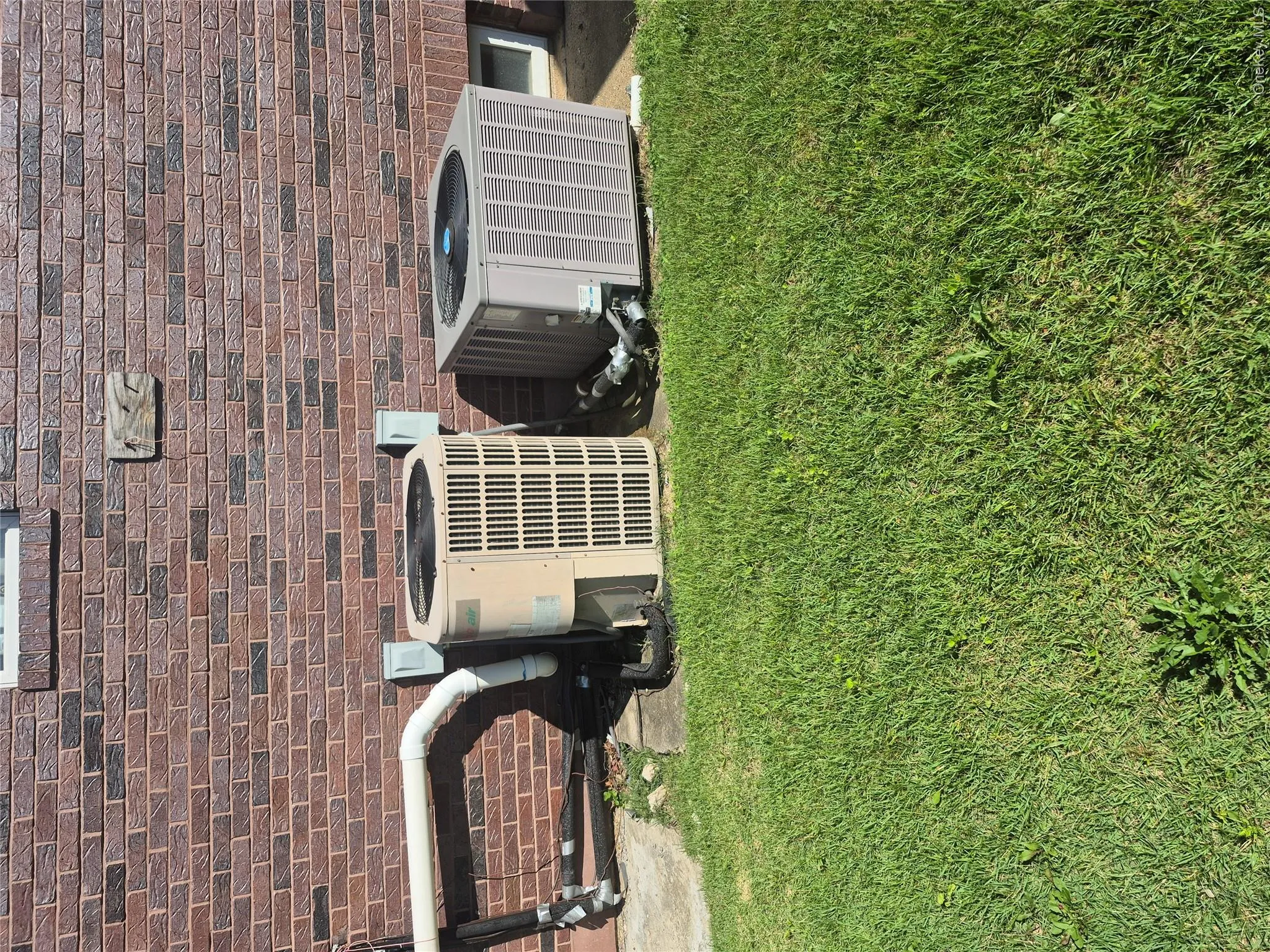Brick exterior with two HVAC units and a ground-level window and landscaped yard area Brick exterior with two HVAC units and a ground-level window and landscaped yard area