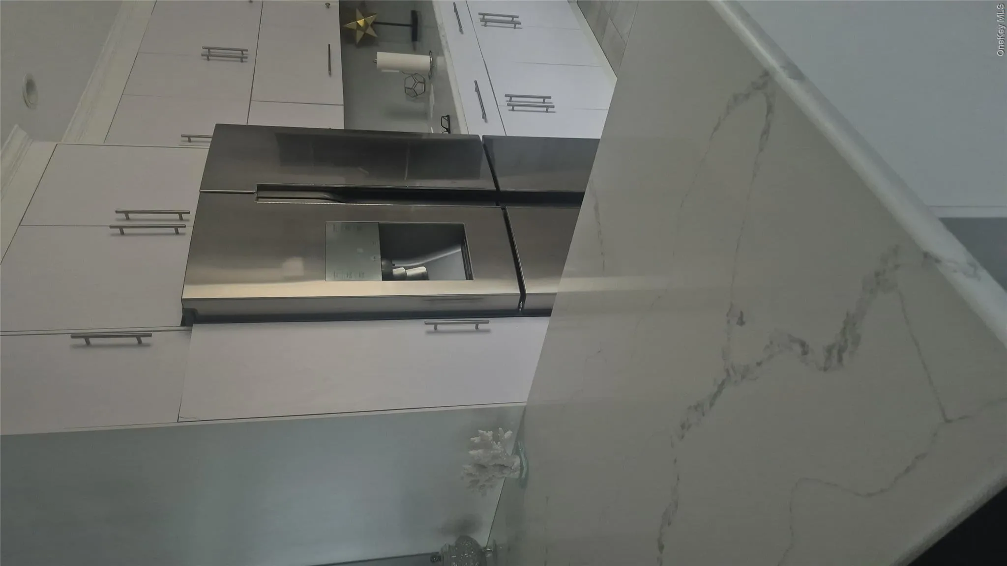 White cabinetry with brushed nickel hardware and stone-finished countertops and bar stools with stainless steel refrigerator White cabinetry with brushed nickel hardware and stone-finished countertops and bar stools with stainless steel refrigerator