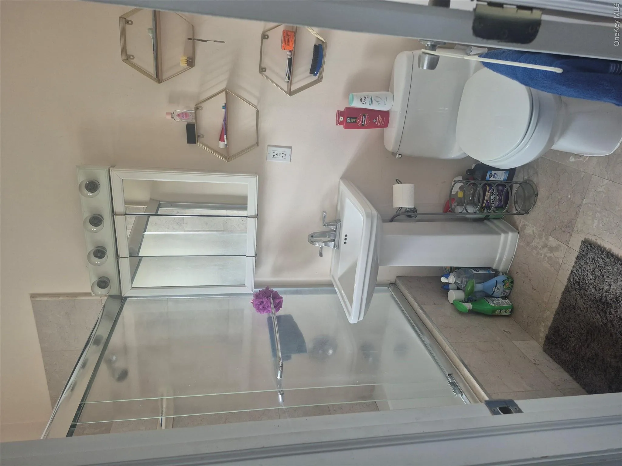 Pedestal sink with chrome faucet, wall-mounted medicine cabinet with integrated lighting, tiled shower surround with glass enclosure, wall-mounted hexagonal shelves, and a white toilet Pedestal sink with chrome faucet, wall-mounted medicine cabinet with integrated lighting, tiled shower surround with glass enclosure, wall-mounted hexagonal shelves, and a white toilet